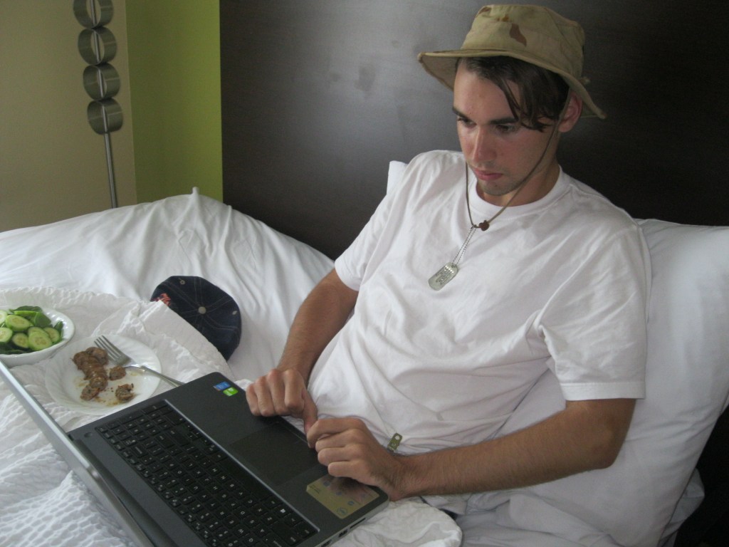 Neil, 19, resting in his Houston hotel room with his laptop, writing a petition to solicit support for his right to continue trying the experimental treatment of his choice. He is wearing a boonie hat and dog tags given to him by a friend who served in the Army Special Forces.